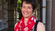 Smiling woman with short hair wearing a red polka dot scarf, standing in an archway.