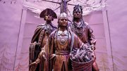 Bronze statues of three historical figures under a stylized tree in a softly lit space.