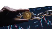 Cryptocurrencies are forms of digital assets stored on blockchains; image depicts hand holding representation of bitcoin over chain