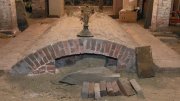 Brick archway with a sandy base, surrounded by wooden planks and boxes in a dim space.