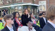 A group of elegantly dressed individuals poses near a parade trolley, smiling and celebrating.