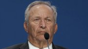Lawrence H. Summers, looking serious while speaking at a podium with a microphone.