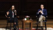 Tina Fey and Robert Carlock seated on stage, engaged in conversation with a small table between them.