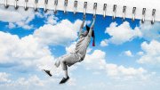 A person hanging from a spiral notebook with a blue sky and clouds in the background.