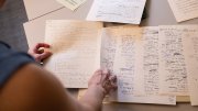 A person examining handwritten notes and papers on a table.