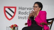 A woman in a pink blazer smiles while seated on stage at a Harvard event.