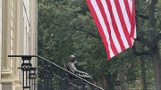 John Harvard statue and the American flag above 