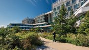 Modern building surrounded by greenery and a walking path under a blue sky.