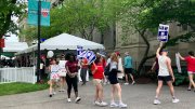 People walking with signs at an outdoor event, near a tent and greenery.
