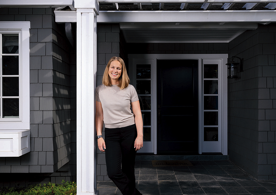Woman in casual attire standing in front of a house's entrance.