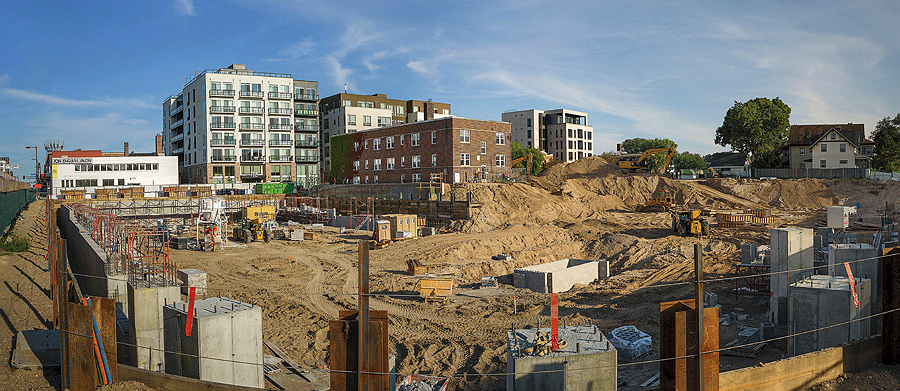 Construction site for a multifamily project with several multi-story buildings in the background.