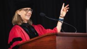 Amanda Claybaugh in academic robes and cap speaking at a podium