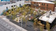 Aerial view of a landscaped area with trees and seating, surrounded by buildings and parking.