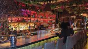 A vibrant bar scene with tropical decor, featuring patrons sitting on high stools.
