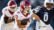 Harvard football player runs with the ball, pursued by opposing players on the field.