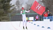 Skier holding a Harvard Crimson flag points at the camera