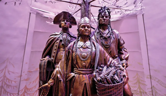 Bronze statues of three historical figures under a stylized tree in a softly lit space.