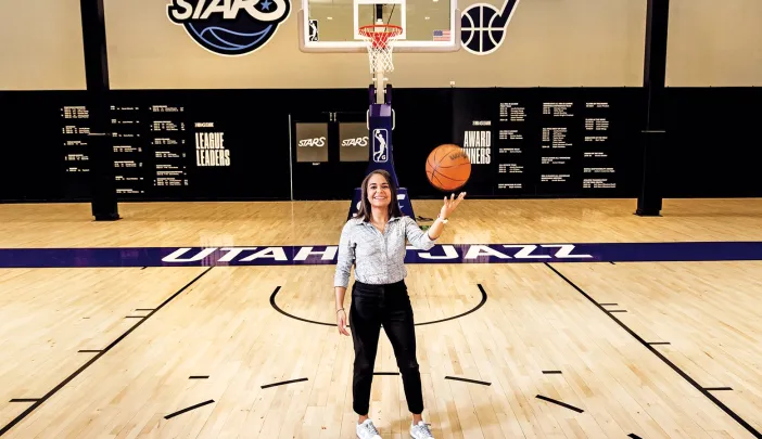 Katie Benzan stands on a basketball court holding a ball, with a hoop in the background.