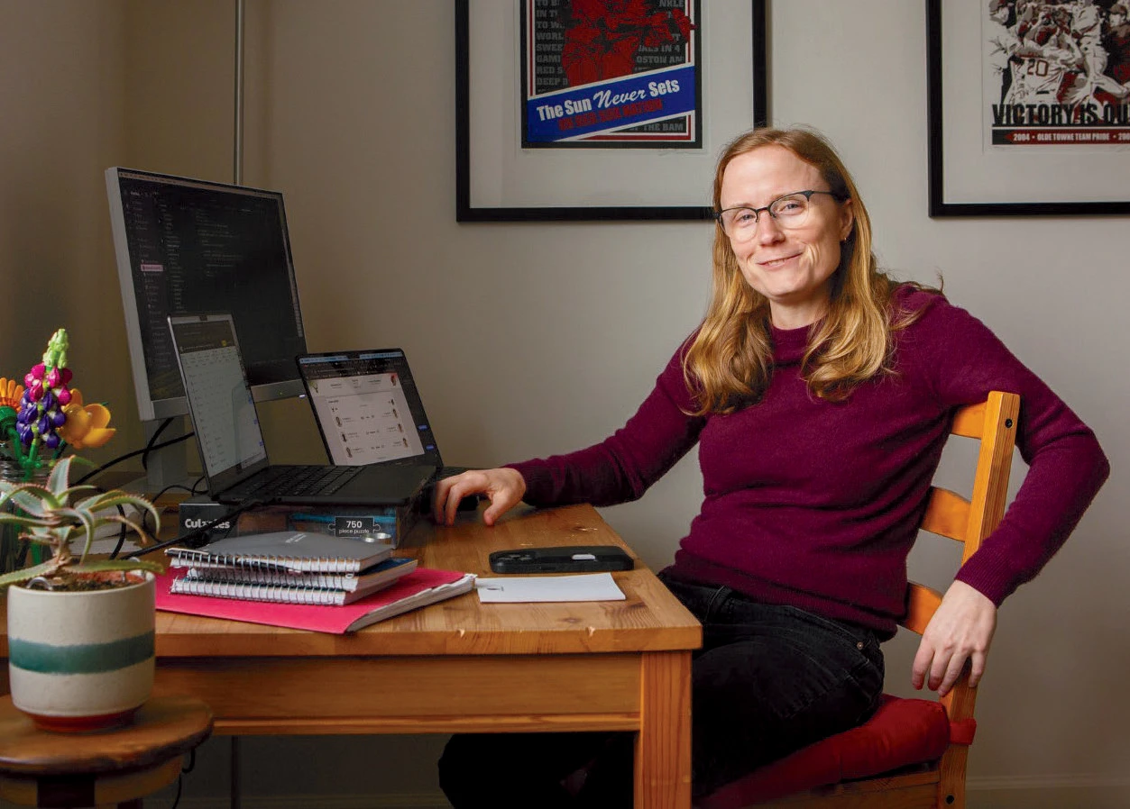 Woman with blond hair and glasses wearing a red sweater sits at a desk with a computer