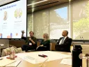 Ned Hall, Rachel Viscomi, and Anthony Foxx speak at a conference table, with a large screen in the background.