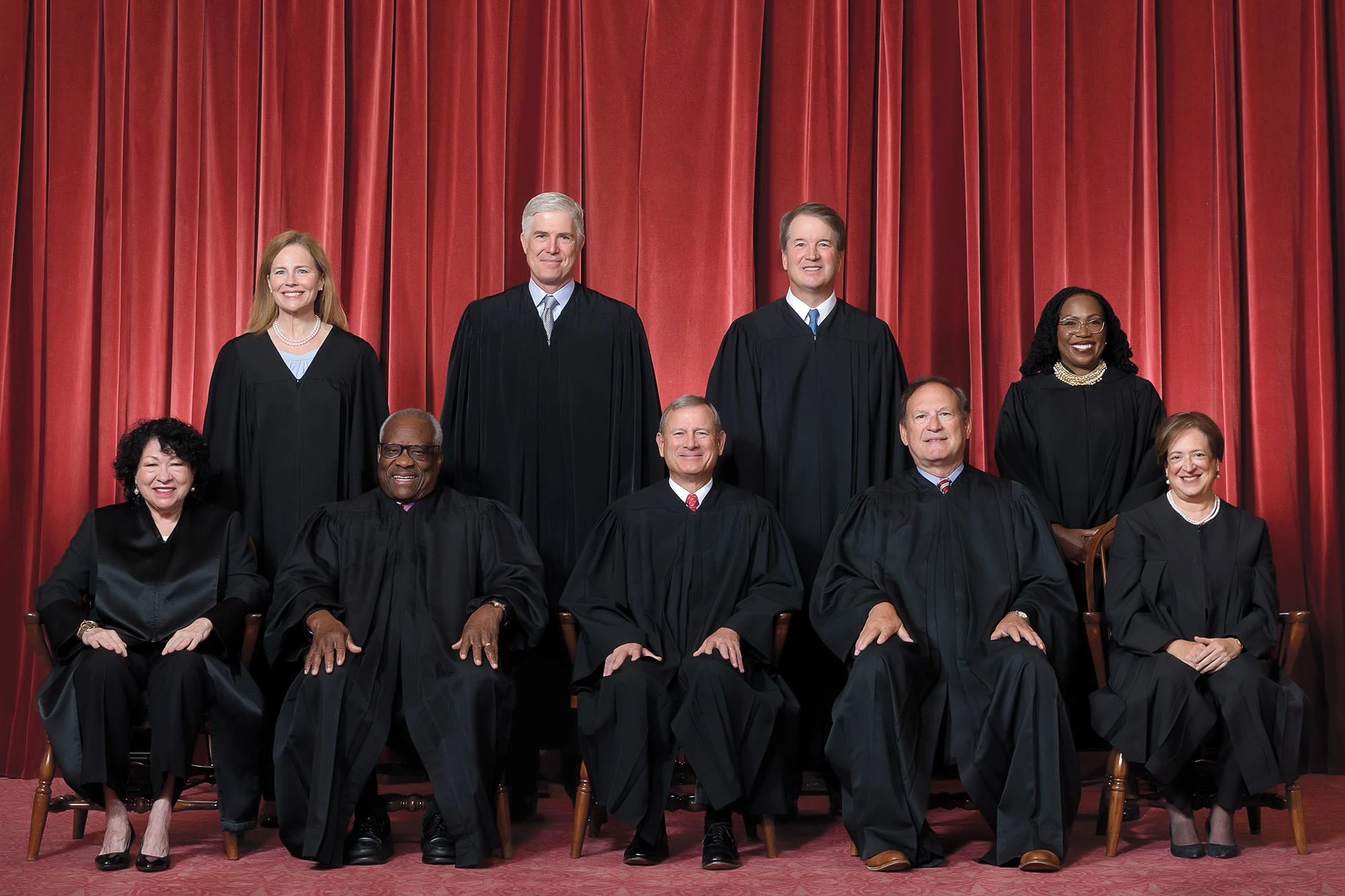 Nine Supreme Court justices posing in front of red curtain.