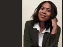 Aisha Muharrar with shoulder-length hair, wearing a green blazer and white shirt.