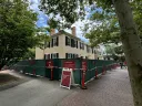 A historic building surrounded by green construction fencing and trees, under a blue sky.