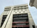 Tall building with multiple stories and large windows, under a cloudy sky.