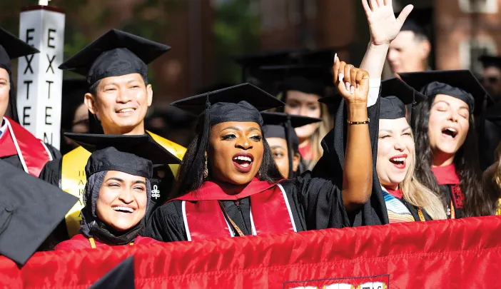 Graduates celebrate joyfully, wearing caps and gowns, with some waving and smiling.