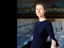 Woman in a navy dress smiling while standing on a walkway with a blurred background.