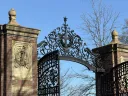 Wrought iron gates with ornate design, framed by brick pillars against a clear blue sky.