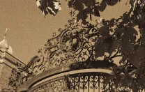 Decorative wrought iron gate framed by leafy branches, captured in sepia tones.