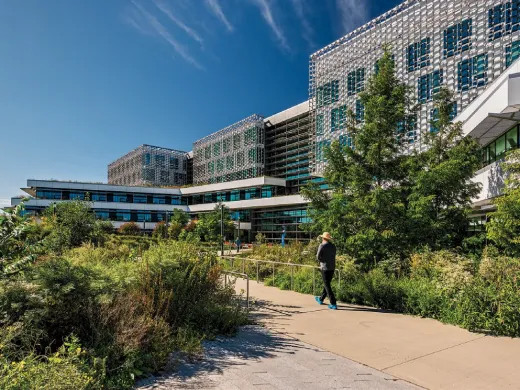 Modern building surrounded by greenery and a walking path under a blue sky.