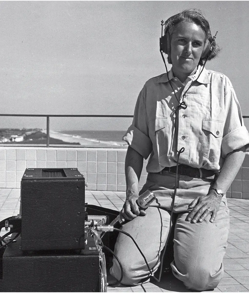 Barbara Lawrence kneeling outdoors in Florida, listening to dolphin vocalizations using headphones and equipment.