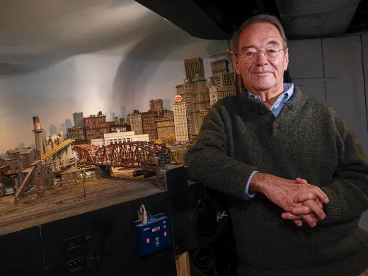 Frank Gevalt standing beside his detailed model city "Port Charles," featuring buildings, bridges, and an urban skyline.