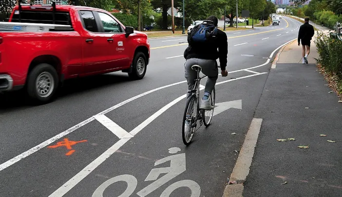 A cyclist rides in a bike lane that ends abruptly near a sidewalk as a red pickup truck passes nearby.
