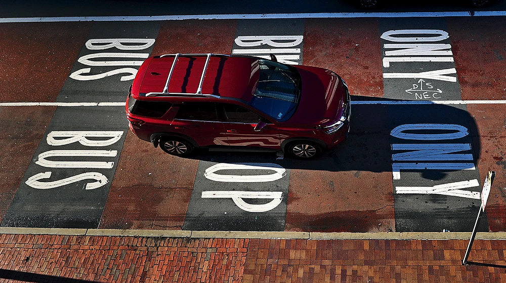 A red SUV drives between two bus-only lanes marked with large white letters on the road in Boston.