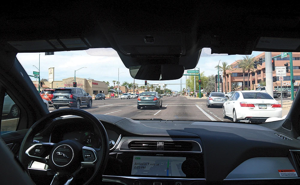 A self-driving Waymo Jaguar taxi navigates a busy Los Angeles street, viewed from inside the vehicle.