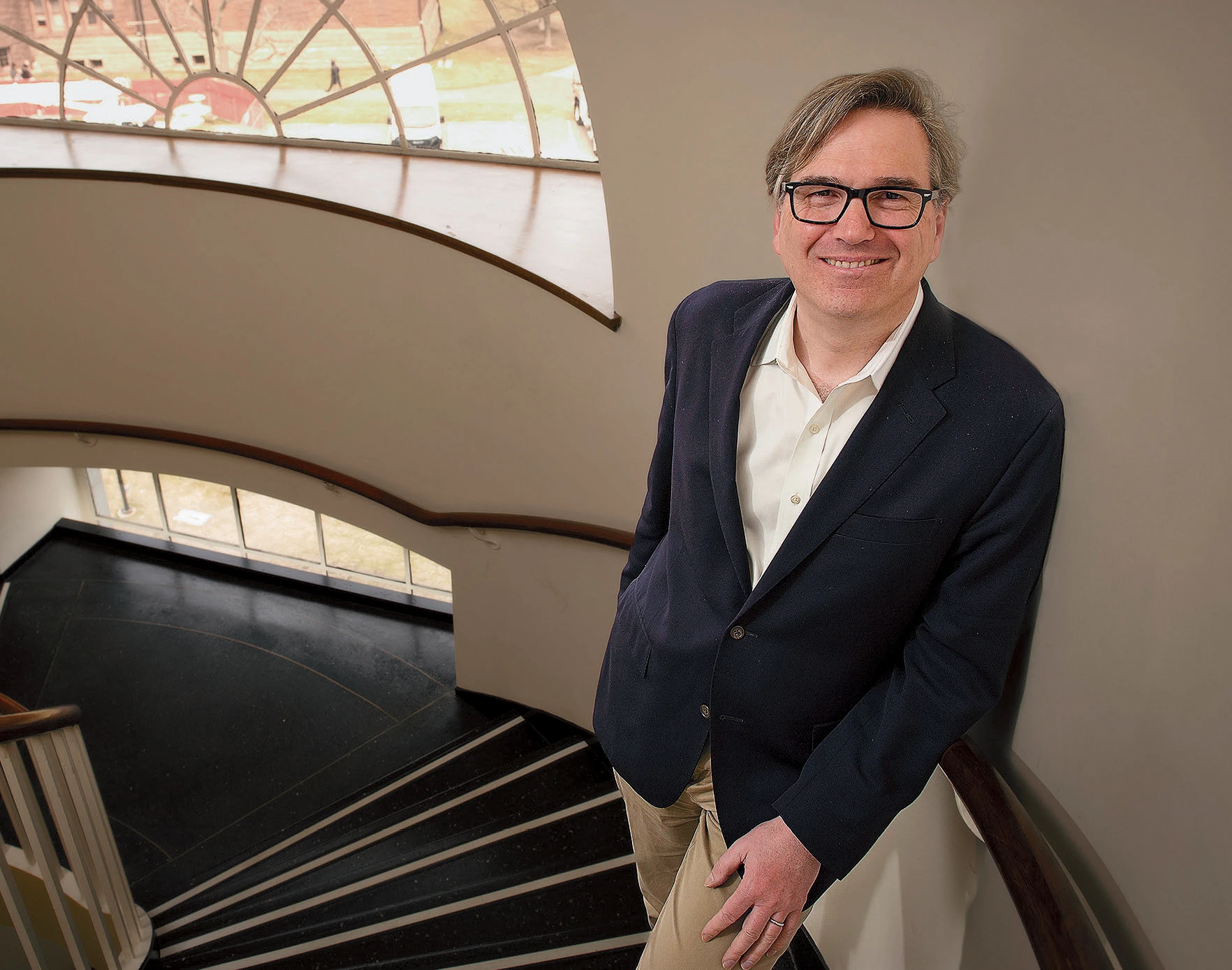 Jason Furman smiling on a spiral staircase, with natural light streaming through an arched window