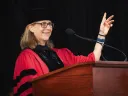 Amanda Claybaugh in academic robes and cap speaking at a podium
