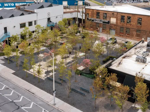 Aerial view of a landscaped area with trees and seating, surrounded by buildings and parking.