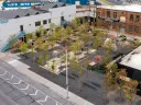 Aerial view of a landscaped area with trees and seating, surrounded by buildings and parking.